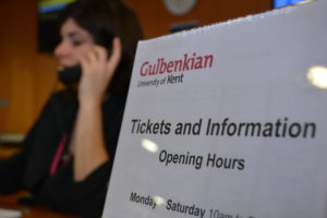 A poster showing Tickets and Information opening times and behind that a member of staff in uniform answering the phone.