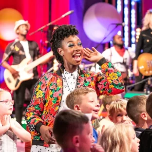 A black woman surrounded by children and a live band