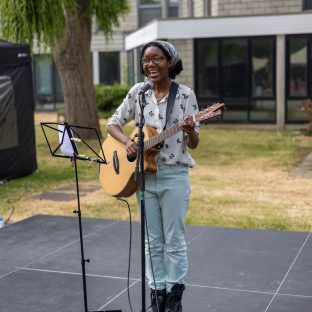 a black woman singing and playing guitar on an outdoor stage