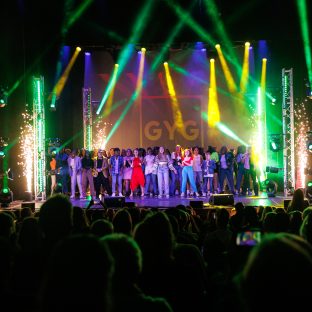 A load of young singers performing on stage with fireworks