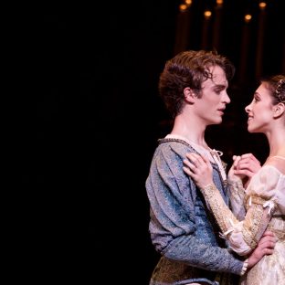 2 ballet dancers holding each other closely, staring into each others eyes lovingly.