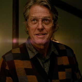 Hugh Grant in 70s glasses with a checkered waistcoat