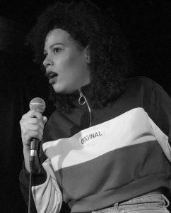 A black and white image of a woman with black curly hair speaking into a microphone